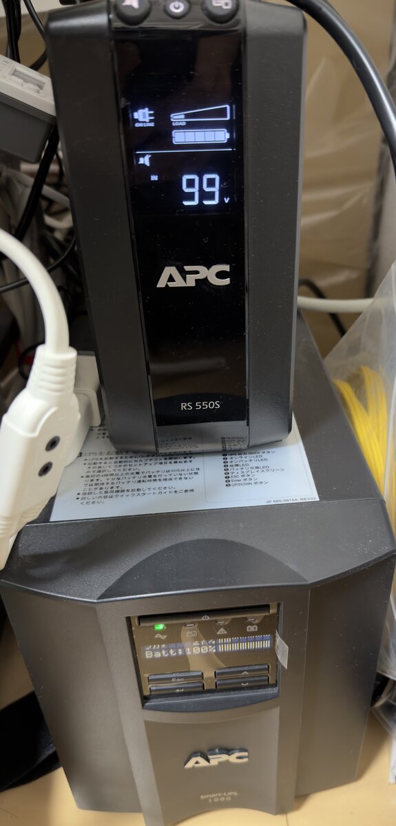 APC UPS 2台の実機。上が RS 550S(BR550S-JP・ライン電圧99Vと負荷を表示中)、下が Smart-UPS 1000(SMT1000J・バッテリ100%表示)